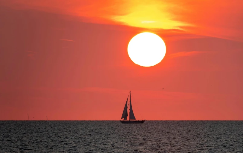 a boat sails away from the setting sun on a body of water