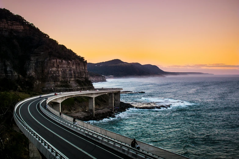 a street next to an ocean with a bridge in the middle