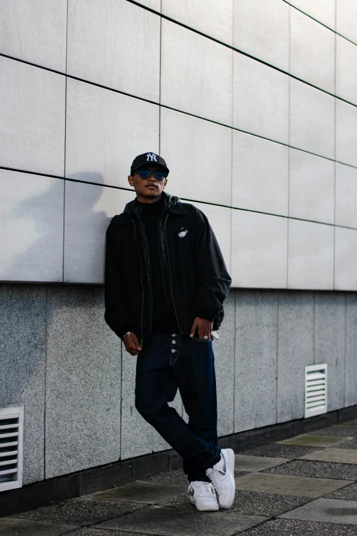 a man leaning against a wall in a black hoodie