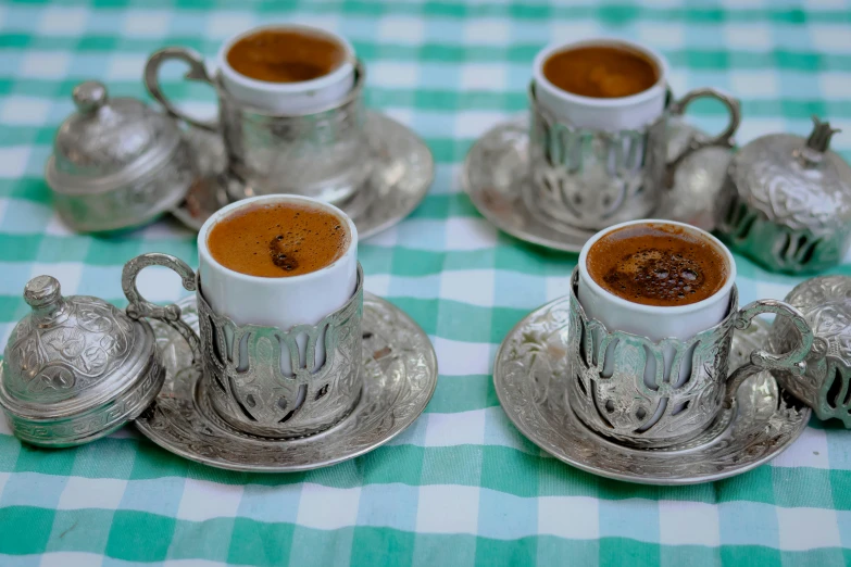 four small tea pots with one full on a tablecloth