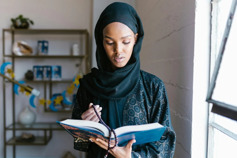 a woman reading a book while wearing a hijab