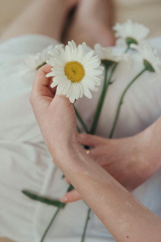 the woman is holding two daisies on her arm