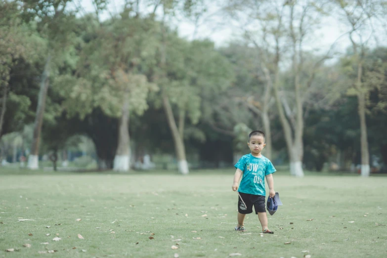 small boy in a blue shirt holding a mitt and standing on grass