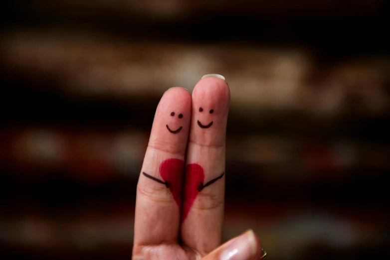 two fingers with drawn hearts, two of them are holding in front of the other, while the other one has a face drawn on its thumb and one