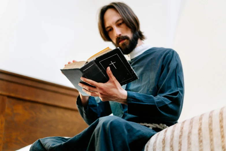 man reading the holy book while sitting on a bed