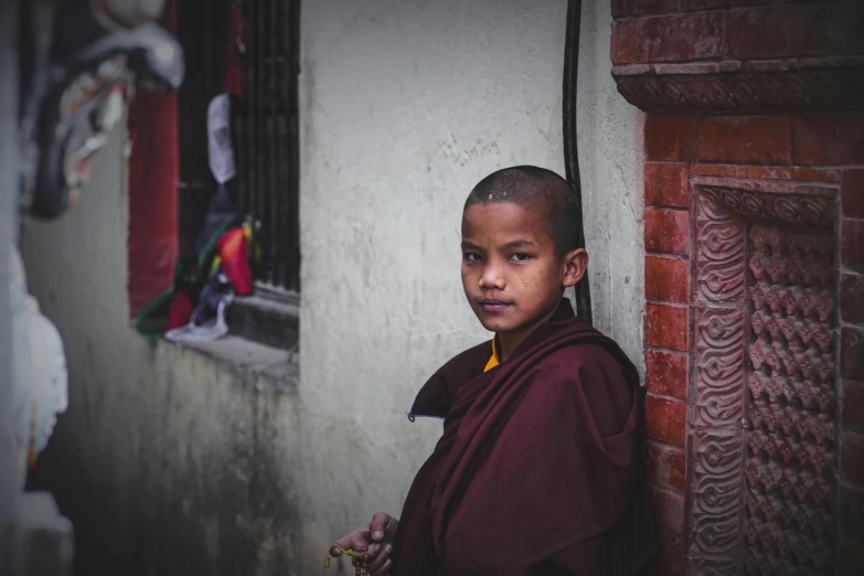 a young monk stands by a wall in the old city