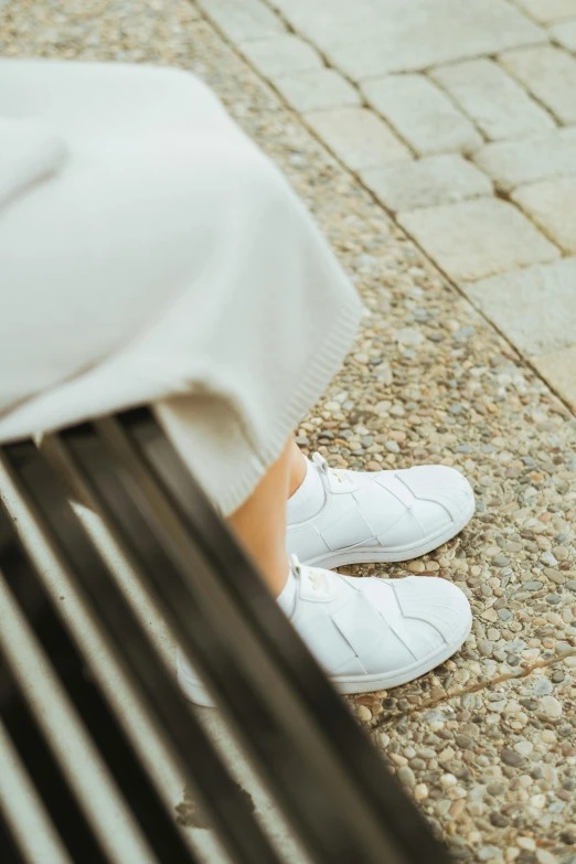 someone in white shoes sitting on a wooden bench