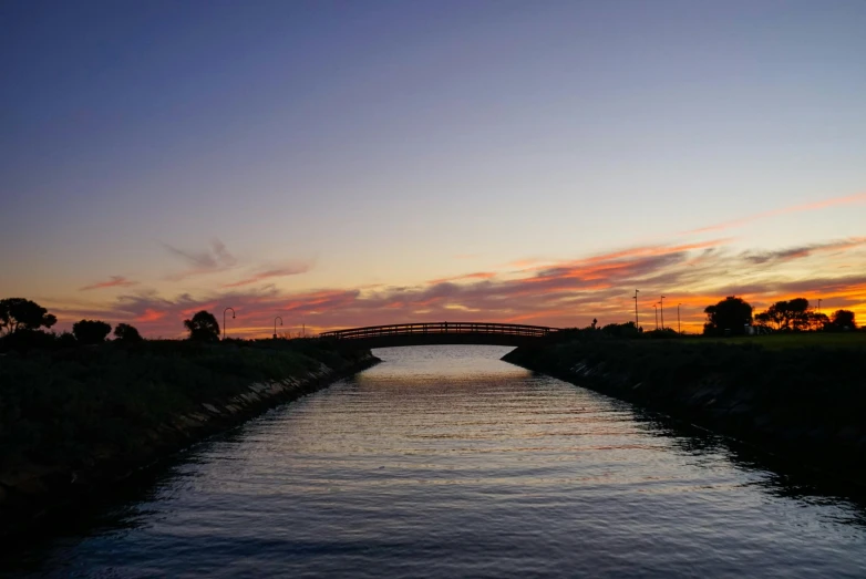 a long river runs under a bridge at sunset