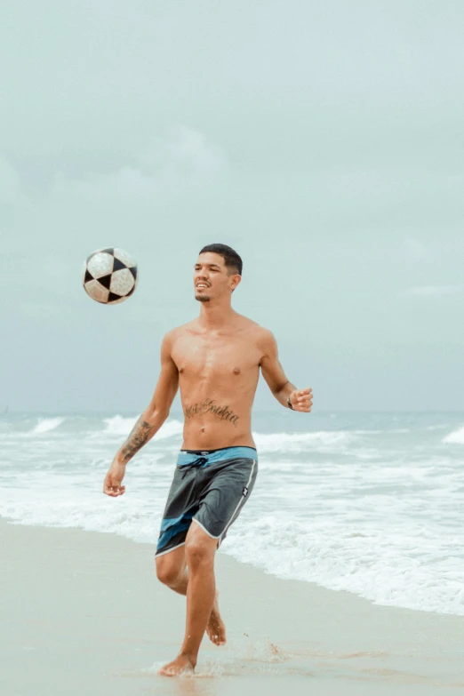 man on beach kicking a ball in the air