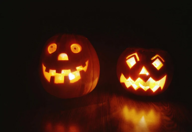 two jack o lantern pumpkins with faces glowing in the dark