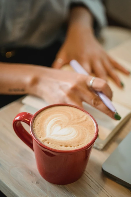 someone's hands, holding a pen, using a laptop with a latte in their hand