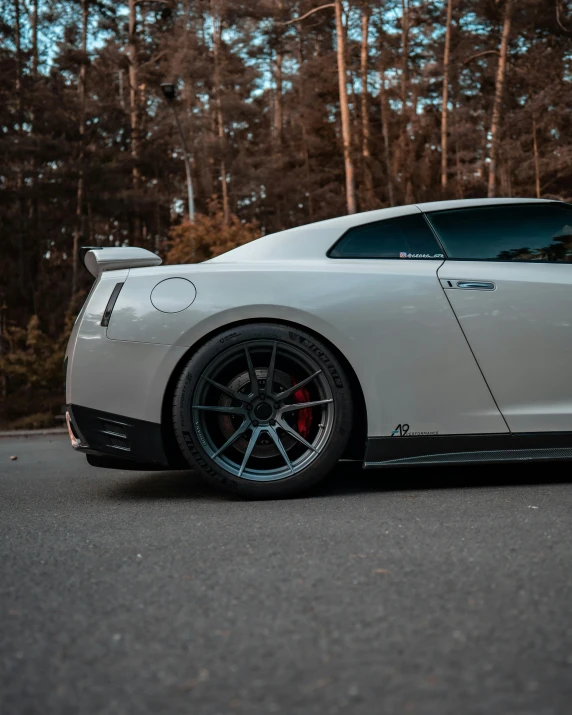 a car that is white with dark rims parked in front of some trees