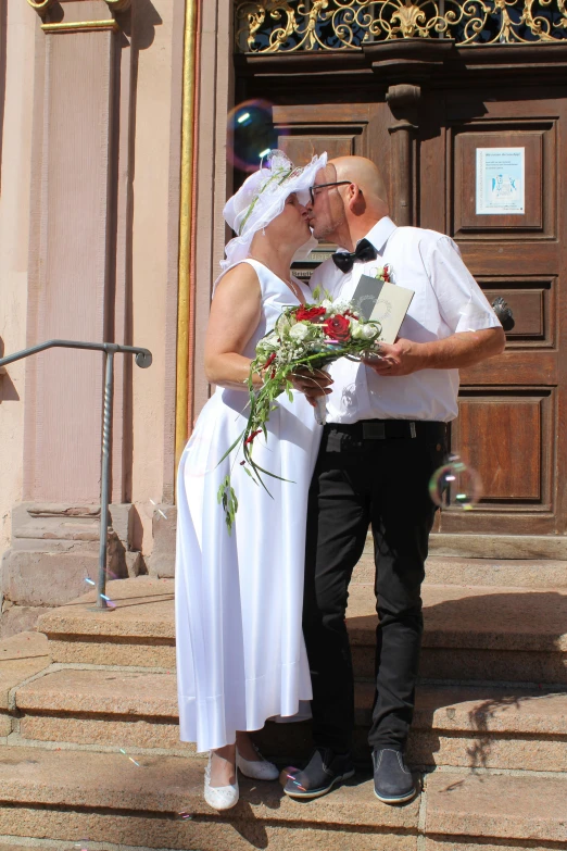 a wedding couple stands on the steps to kiss