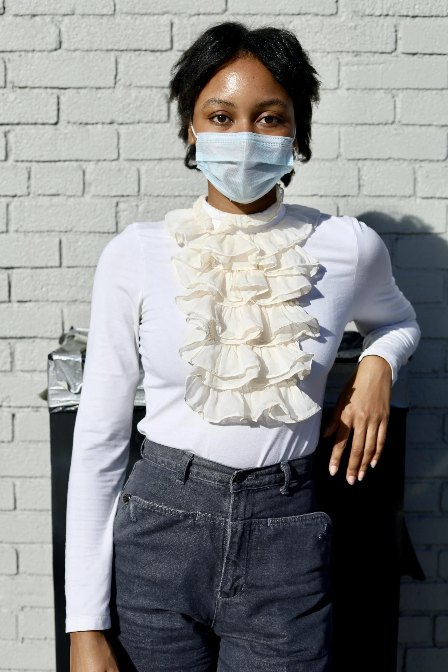 a young woman in white shirt and black pants wears a mask