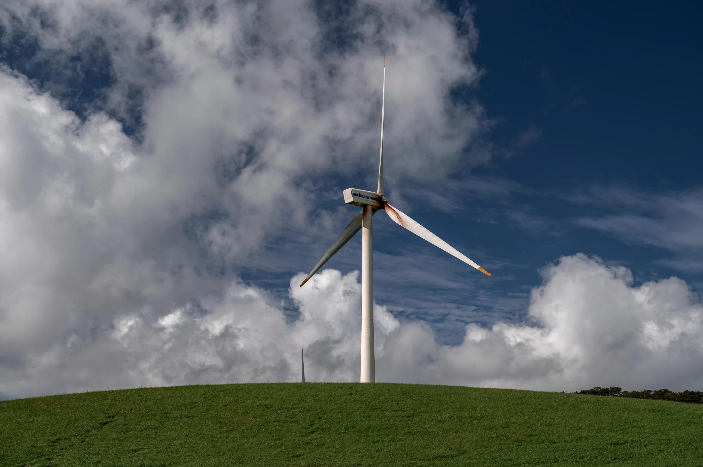 a wind turbine sticking from the side of a tall green hill