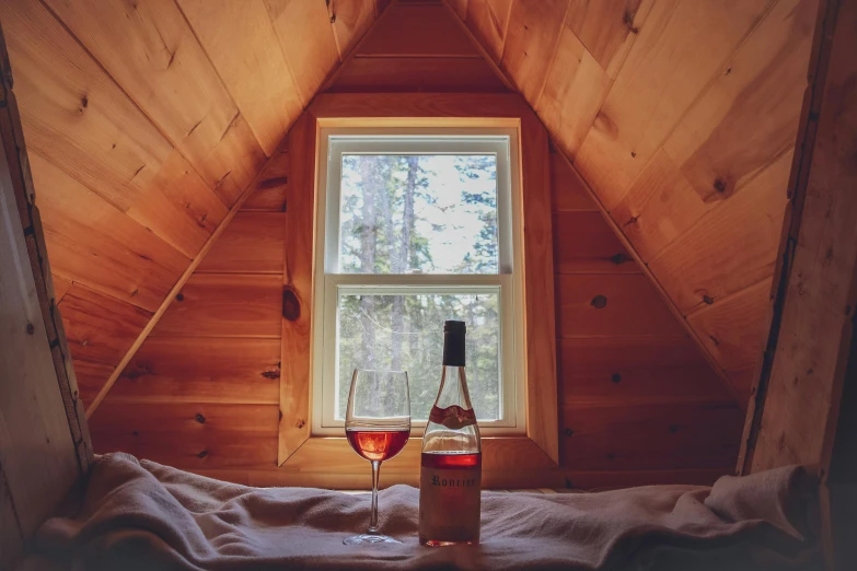 the inside of a cabin with a window and a bottle of alcohol on a blanket in front of it