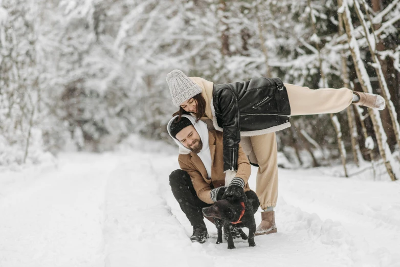 man and woman petting black dog in snow