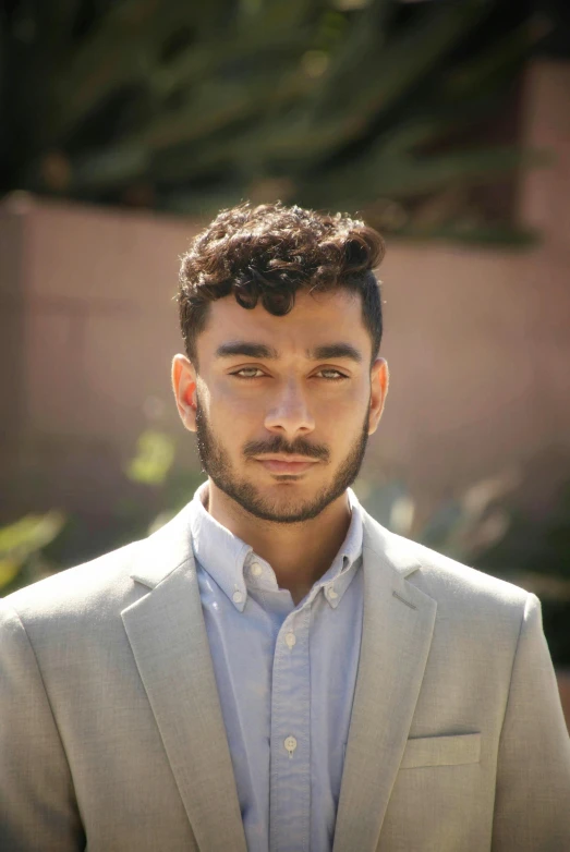 a young man looks at the camera as he stands in front of trees