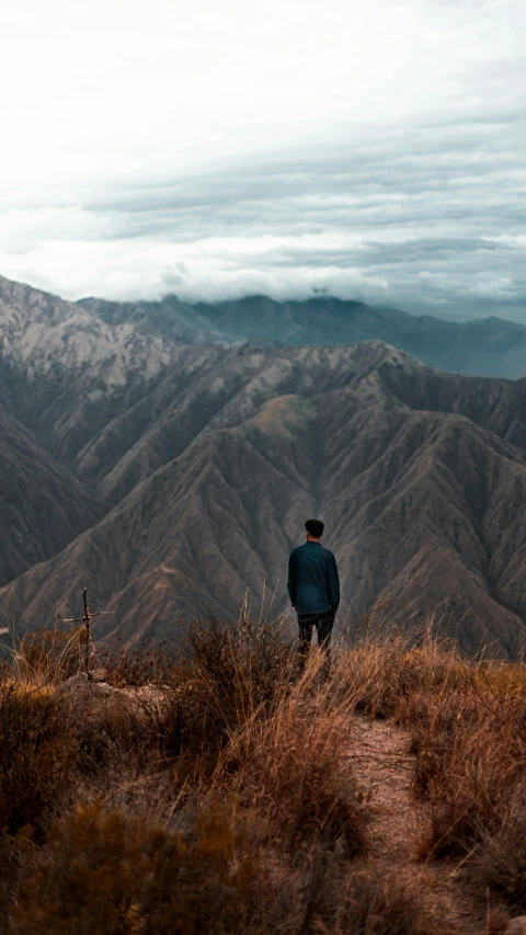 a man stands atop a hill overlooking mountains and clouds