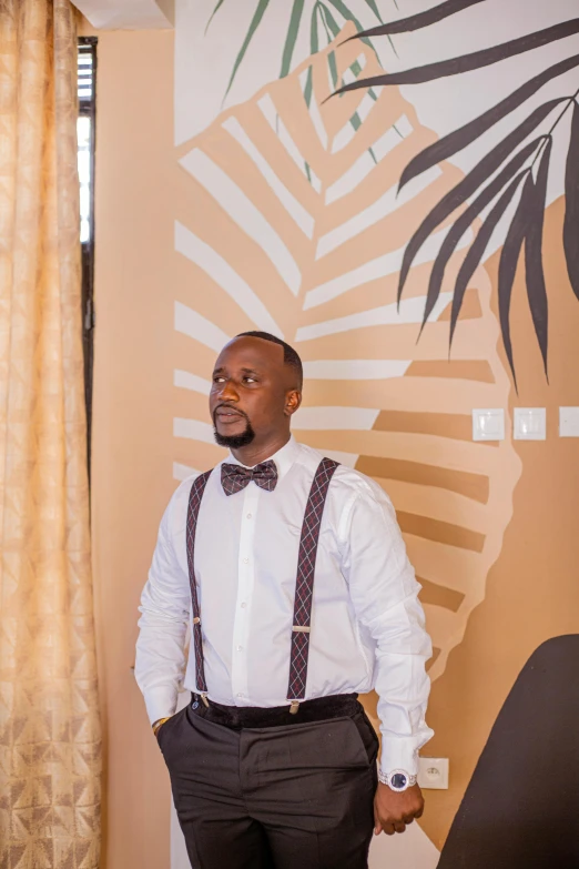 a man wearing a bow tie and suspenders in front of a wall with tropical designs