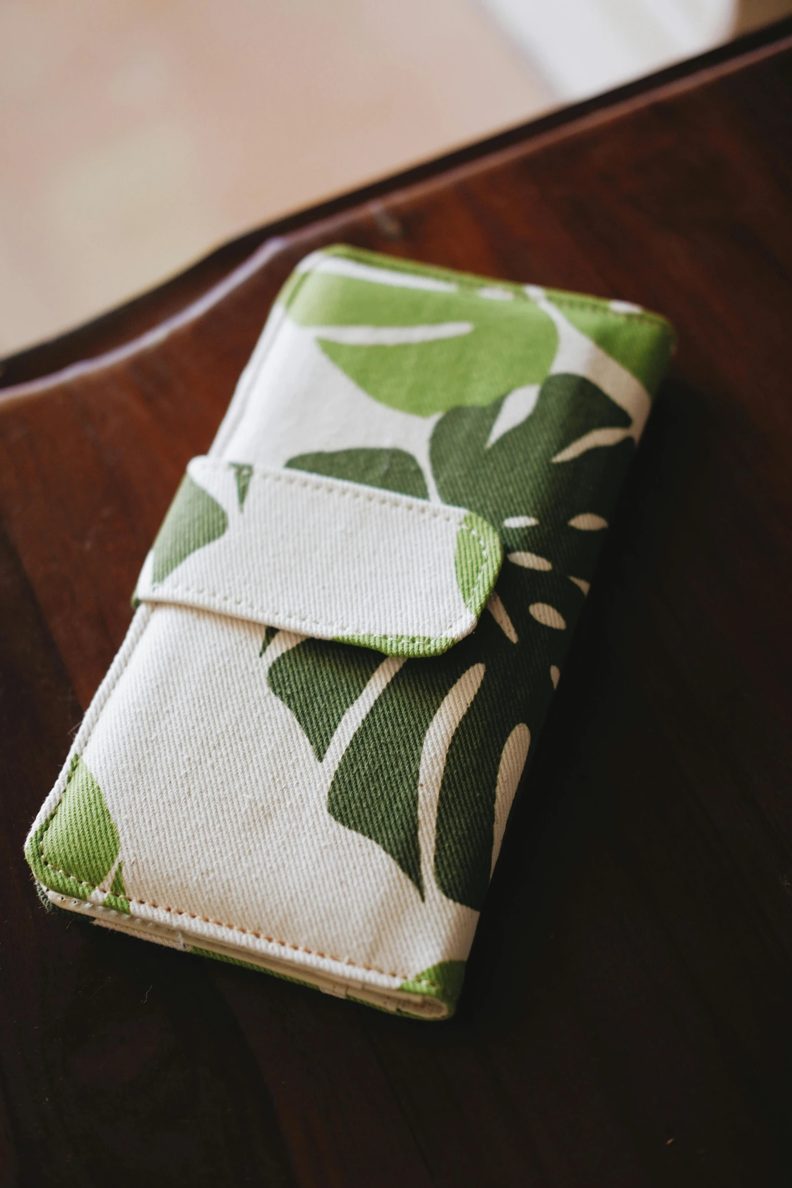 a white and green floral print purse sitting on top of a wooden table