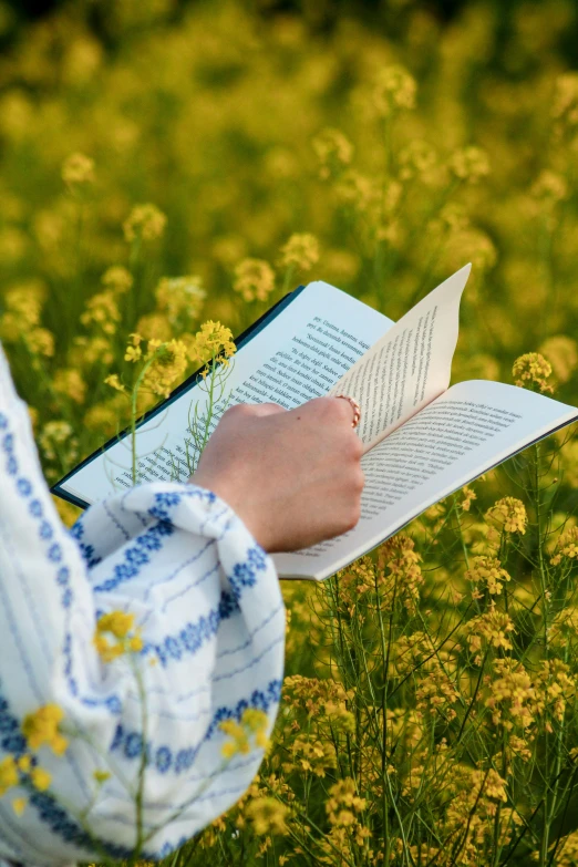 a person holding a book in front of some flowers