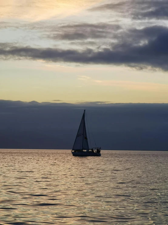 a sailboat sailing across the ocean with a cloudy sky behind it