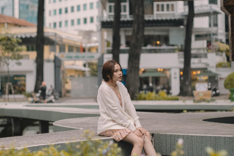 the woman is sitting on a cement bench in front of buildings