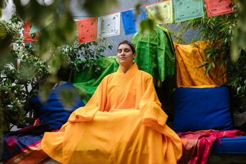 a man with yellow robes sitting on a mat outside