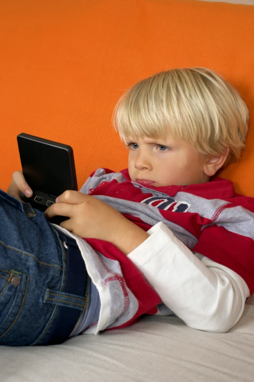 small child laying down on the bed using a cellphone