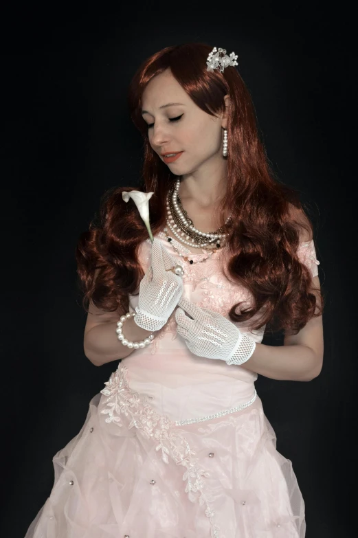 a woman with long hair and pearls holds up an object in her hands