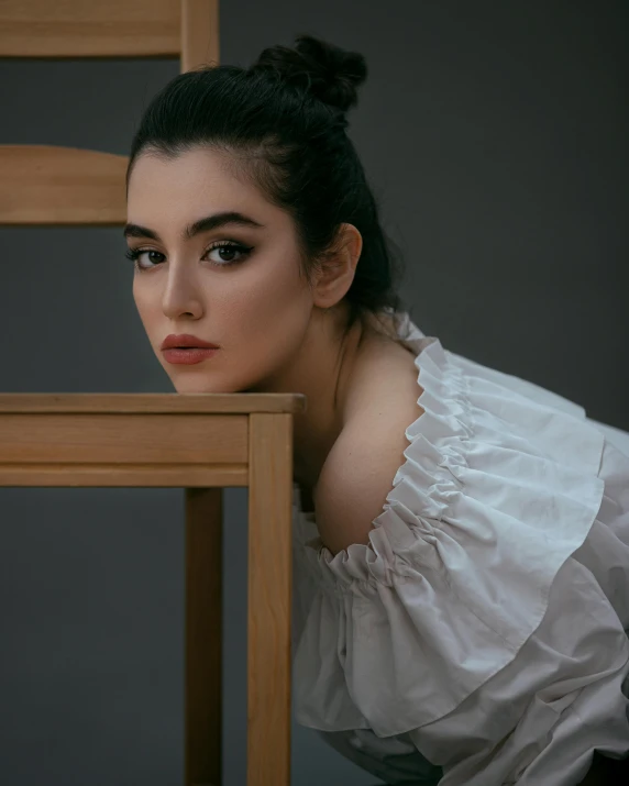 a woman with dark hair is wearing a white shirt and sits at the wooden chair