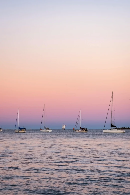 four small boats floating on top of the ocean at dusk