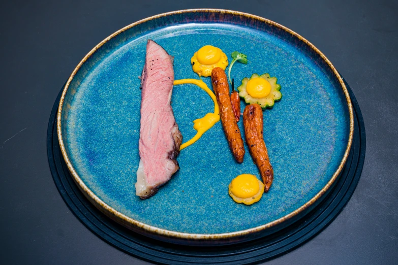 a blue plate with a carrot and two other meats on it