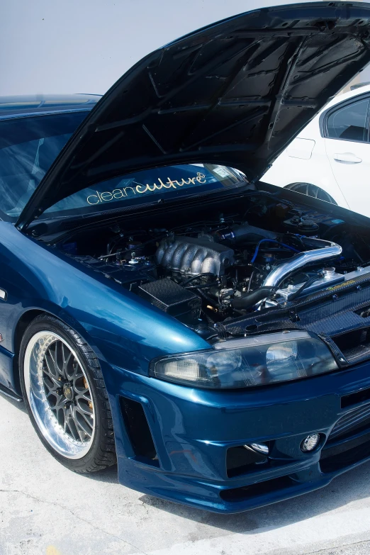 a blue car with its hood down sitting next to another car