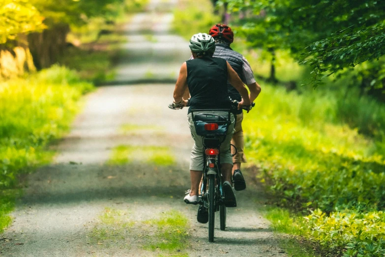 two people riding bikes on a pathway with trees in the background