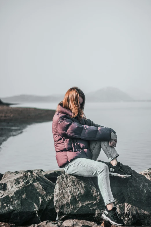 the person is sitting on the rocks looking out at the water