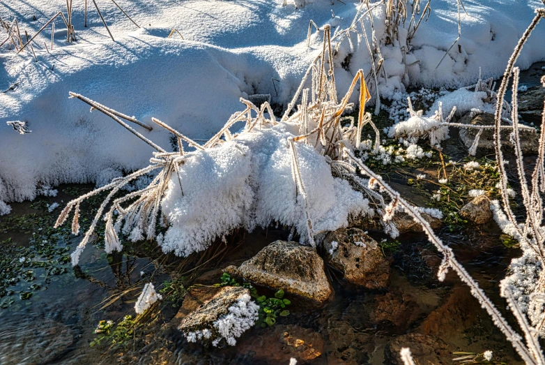 there is snow on the ground and water next to the rocks