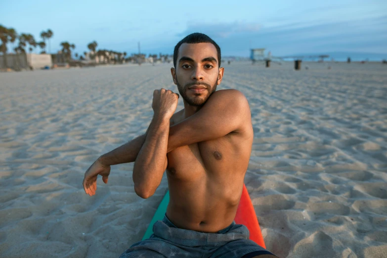 a man that is sitting down in the sand with a board