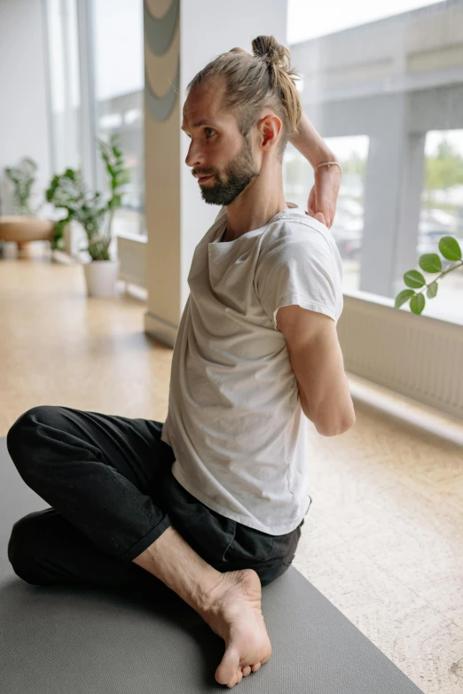 a man sitting on a yoga mat with his hair pulled back