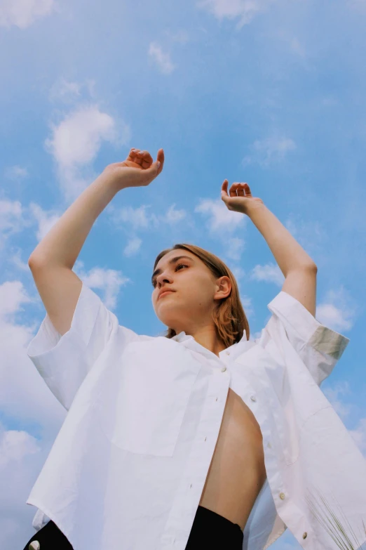 a woman standing with her arms up wearing a white blouse and black pants