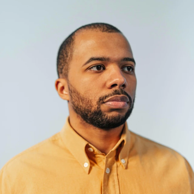 a man in a mustard colored shirt looking up with serious eyes