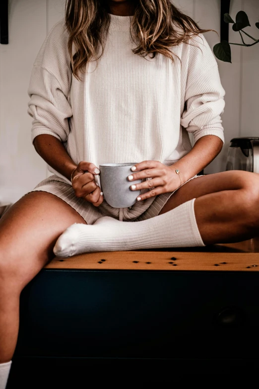 woman sitting on a kitchen counter holding a coffee cup