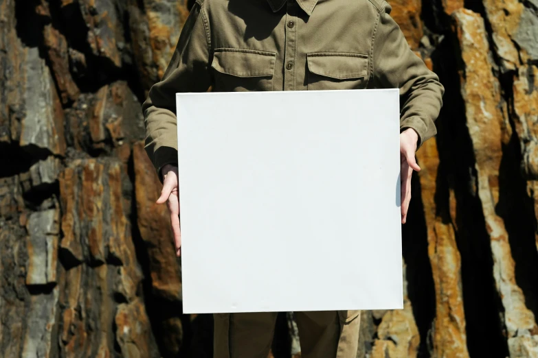 man holding up white paper in front of large rocks