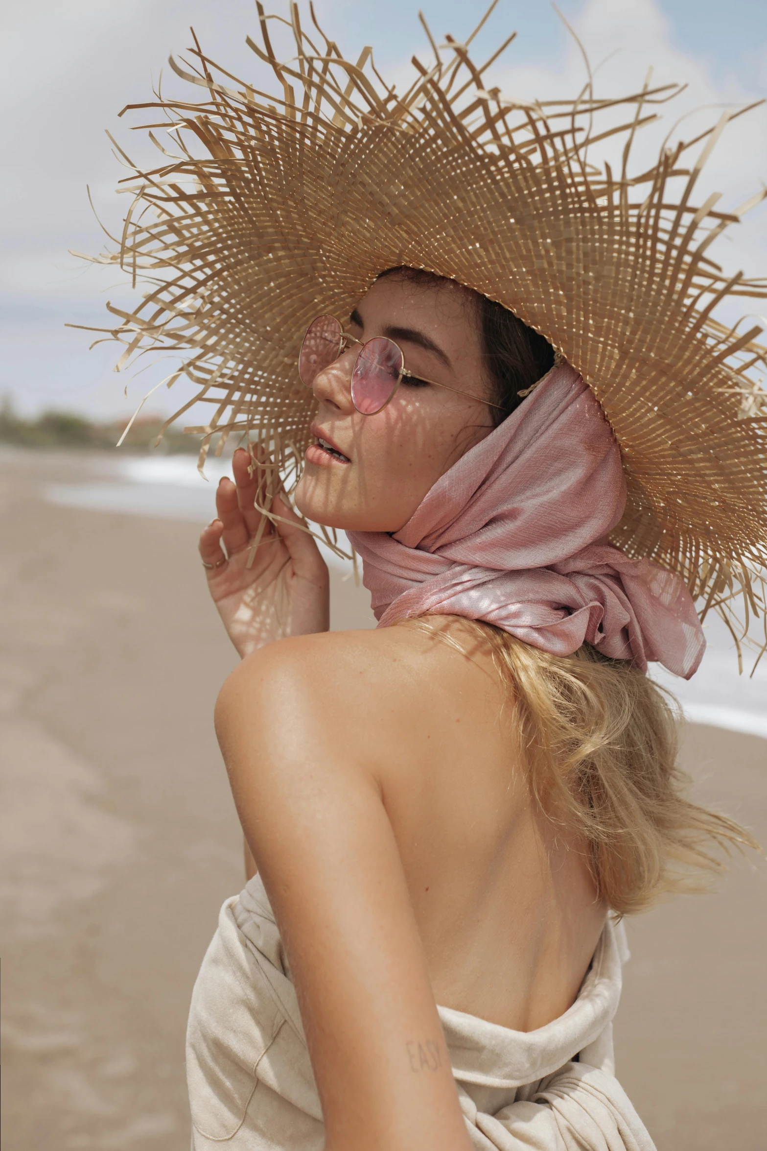 a young woman standing on the beach with her face covered by straw hat