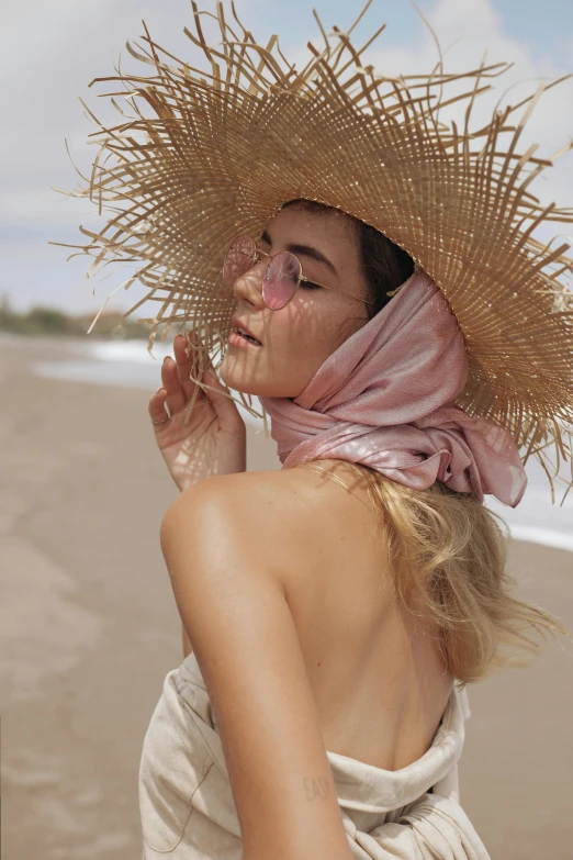 a young woman standing on the beach with her face covered by straw hat