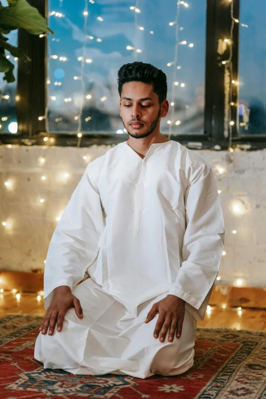 a man sits in a white outfit on a rug