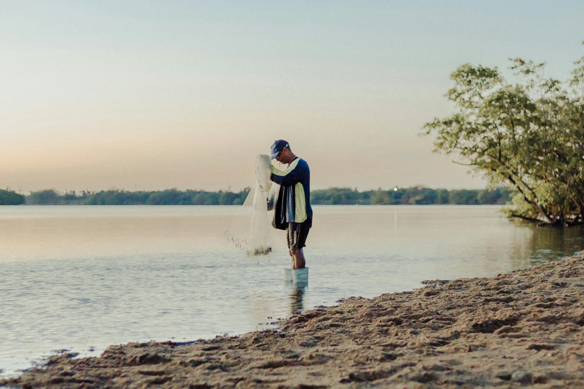 a man holding a fish while standing on top of a sandy shore