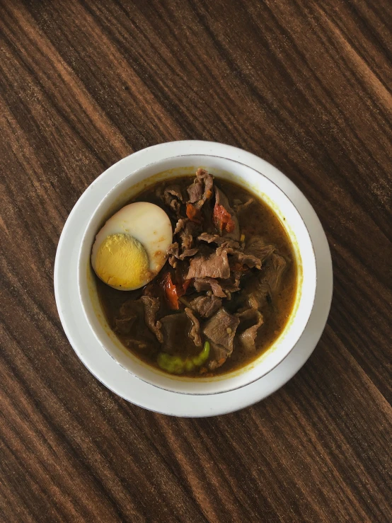 bowl with soup and two pieces of meat inside of it on wooden table