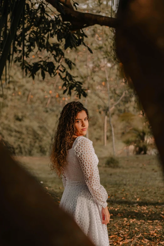 a  wearing a dress is smiling while standing under a tree